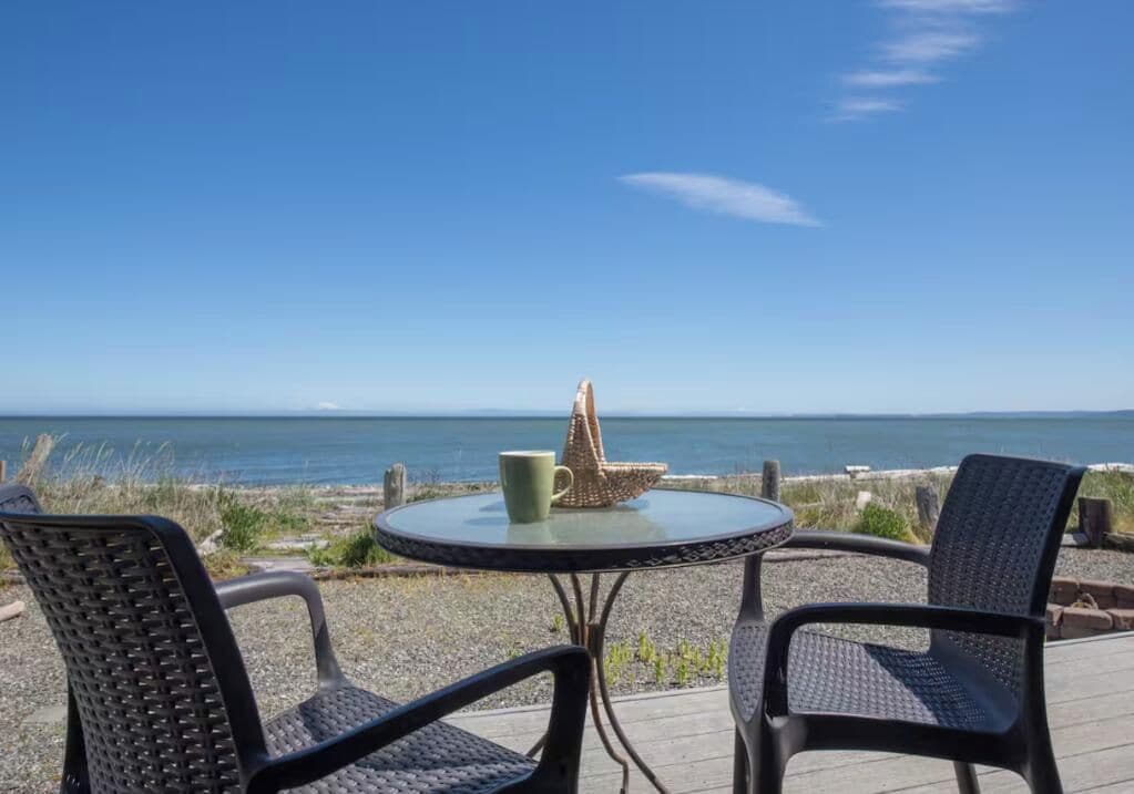 Een ronde tafel met twee stoelen en een decoratief object, met uitzicht op een strand en de oceaan.