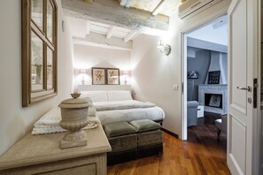Una camera da letto con un letto, lampade sui comodini, un vaso in pietra e una porta che dà su un'altra stanza.