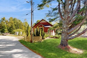 A red house with a sloped roof, surrounded by a well-maintained lawn and a large tree. - Cozy Ludlow Cottage | Minutes to Okemo & Year-Round Adventure (Ludlow)