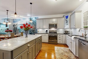 A modern kitchen with a large island, stainless steel appliances, and a decorative mural. - Cozy Ludlow Cottage | Minutes to Okemo & Year-Round Adventure (Ludlow)