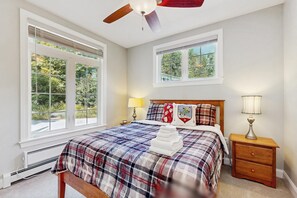 A bedroom with a bed, two windows, a ceiling fan, a nightstand, and a lamp. - Cozy Ludlow Cottage | Minutes to Okemo & Year-Round Adventure (Ludlow)