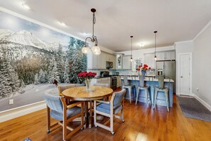 A modern kitchen with a dining area, featuring wooden flooring, a round table with chairs, and a mural of a snowy landscape on the wall. - Cozy Ludlow Cottage | Minutes to Okemo & Year-Round Adventure (Ludlow)