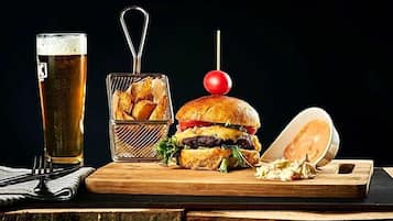 Una comida con una hamburguesa, papas fritas y una bebida sobre una mesa de madera.
