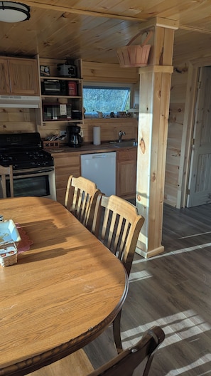 Ein Holzinterieur mit Esstisch, Stühlen, einer Küchenzeile inklusive Geräten und einem Fenster.
