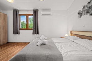 A hotel room with a bed, a window with curtains, an air conditioning unit, a wooden wardrobe, and a wall-mounted artwork. - Villa Nina u Poreču, Istra by Istrabook (Poreč)