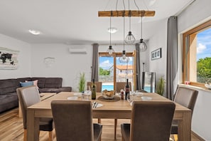 A dining area with a wooden table, chairs, and hanging pendant lights. - Villa Nina u Poreču, Istra by Istrabook (Poreč)