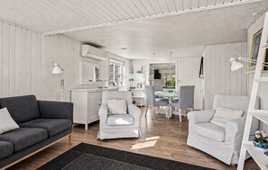 A modern living room with a grey sofa, two white armchairs, a dining area with a table and chairs, and a kitchen area with a fridge and microwave. - 2 bedroom beautiful home in Ebeltoft (Ebeltoft)