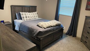 Un dormitorio con cama, mesita de noche, cómoda y ventana con cortinas.