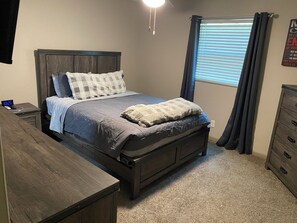 Un dormitorio con cama, mesita de noche, cómoda y ventana con cortinas.