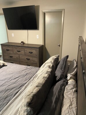 Un dormitorio con cama, cómoda y televisor montado en la pared.