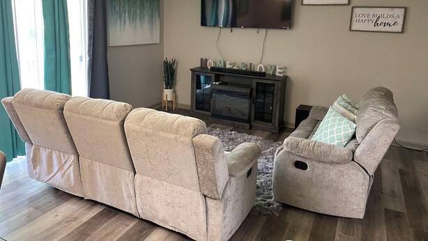 Una sala de estar con dos sofás beige, un televisor de pantalla plana montado en la pared y una chimenea con repisa.