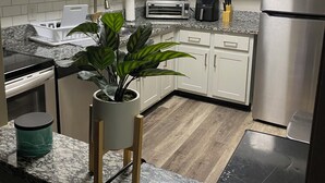Una cocina moderna con armarios blancos, un refrigerador de acero inoxidable, un microondas, un tostador y un lavamanos.