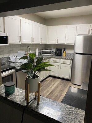 Una cocina moderna con armarios blancos, un refrigerador de acero inoxidable, un microondas, un tostador y un lavamanos.