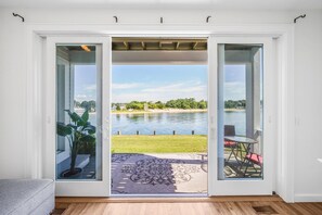 Eine Glastür führt zu einer Terrasse mit Blick auf einen See, eine Rasenfläche und eine Sitzecke.