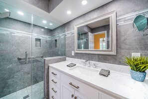 Un bagno moderno con cabina doccia in vetro, uno specchio grande e un mobile lavabo bianco.