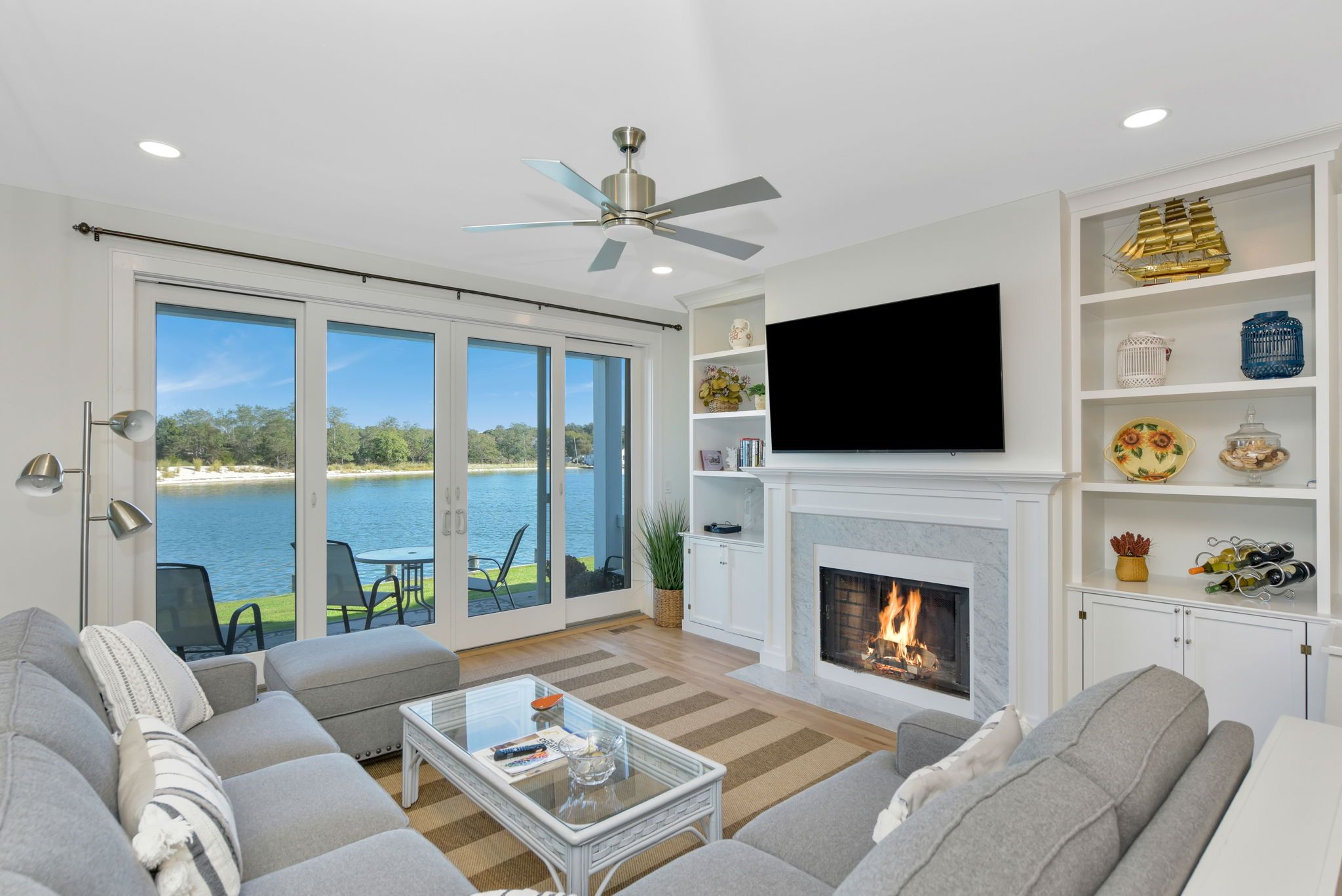 A modern living room with a fireplace, a flat-screen TV, and a view of a body of water through large sliding doors.