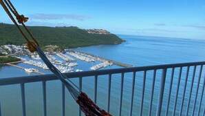 Marina com barcos atracados, cidade costeira ao fundo e céu claro.