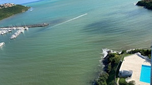 Marina com barcos atracados, um cais que se estende na água e um edifício com piscina.