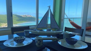 Uma sala de jantar com mesa posta para dois, vista para o oceano e uma rede na varanda.