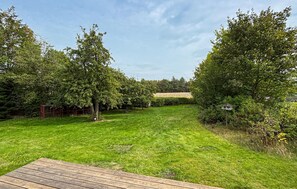 Un giardino sul retro con prato, un patio in legno, alberi e una casetta per uccelli.