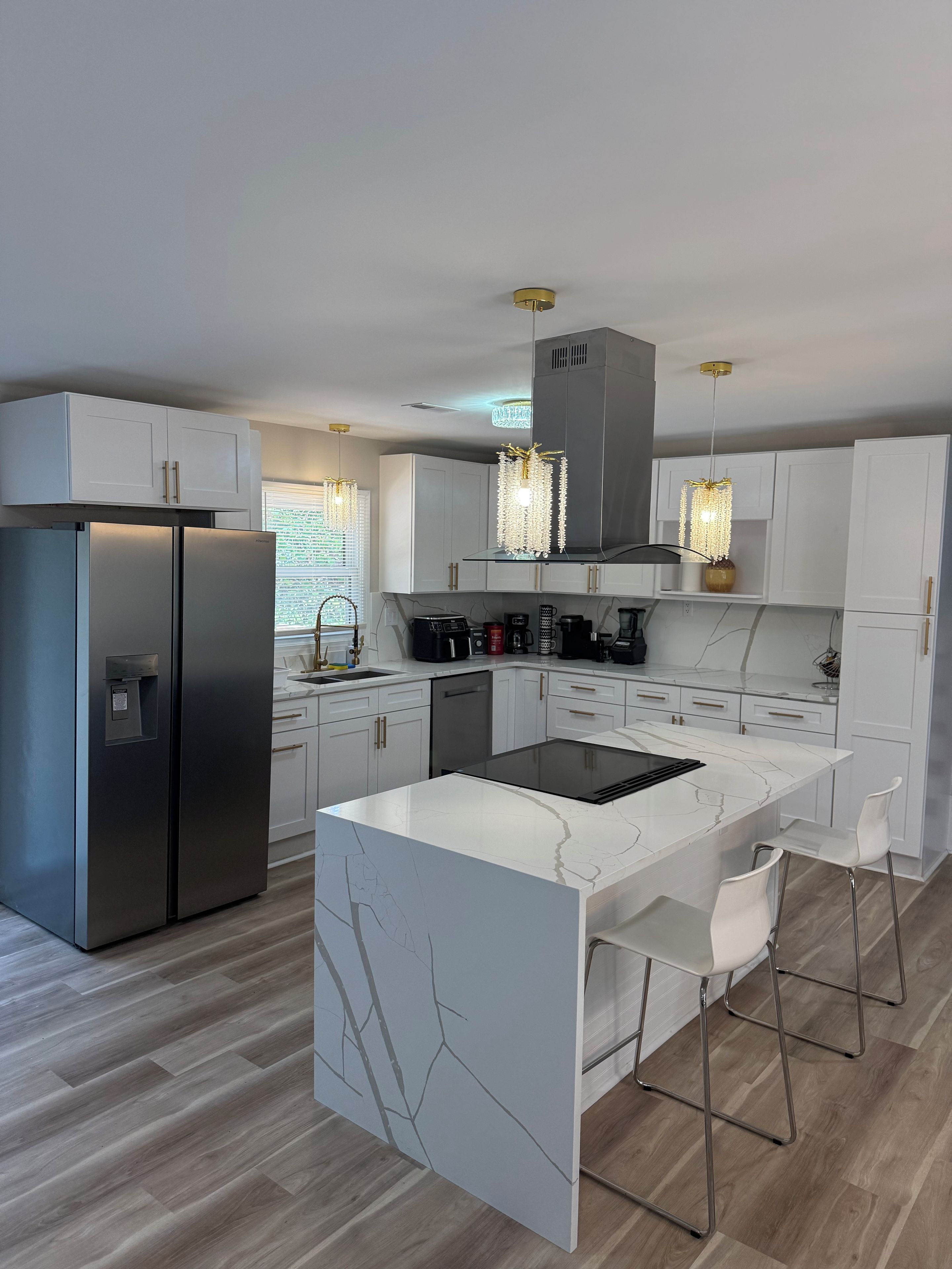 Une cuisine moderne dotée d’un îlot central, d’appareils électroménagers en acier inoxydable et de luminaires suspendus.