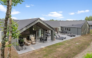 Ein modernes Haus mit überdachter Terrasse, Gartenmöbeln und einer Grillgelegenheit.