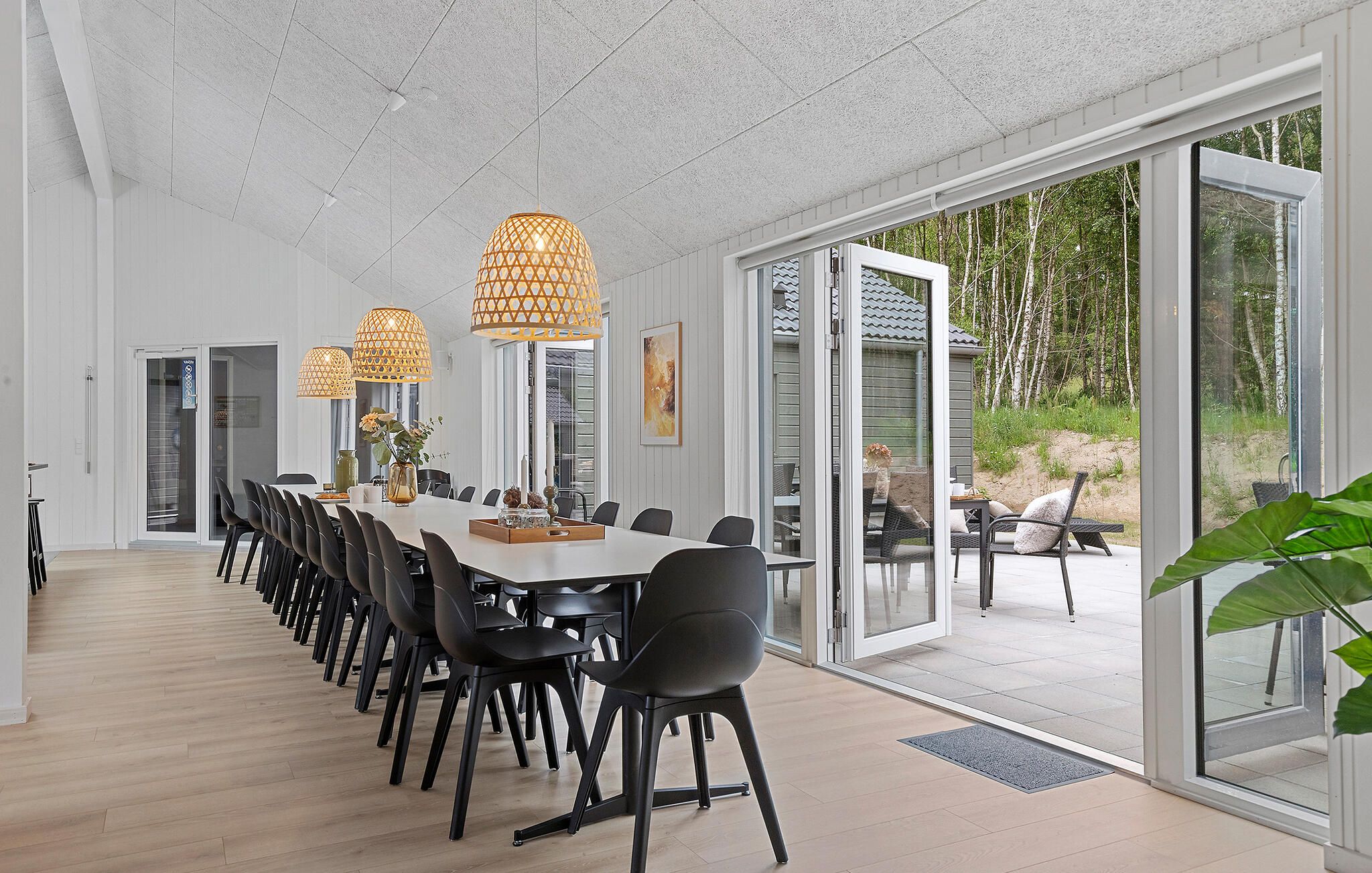 Een ruime eetruimte met een lange tafel, zwarte stoelen en hanglampen.