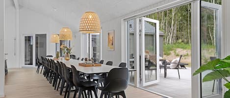 A spacious dining area with a long table, black chairs, and pendant lights.