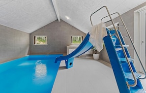 Ein Hallenbad mit einer blauen Rutsche, einer Leiter und zwei Fenstern.