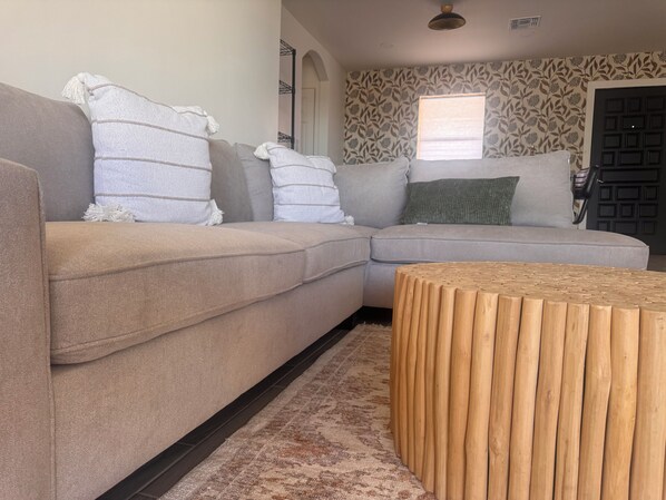 A modern living room with a beige sectional sofa, a wooden coffee table, and patterned wallpaper.