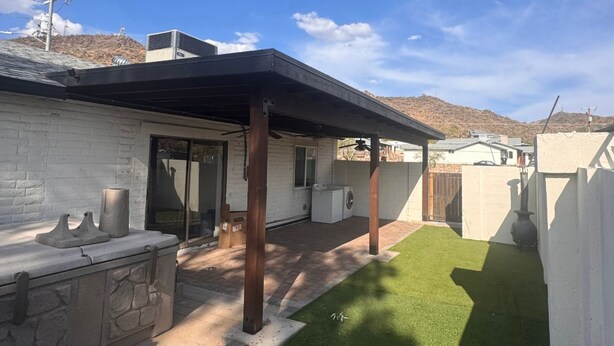 Ein Garten mit künstlichem Rasen, einer Steinbank und einer überdachten Terrasse.