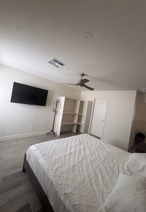 A bedroom with a bed, a wardrobe, a ceiling fan, and a TV mounted on the wall.