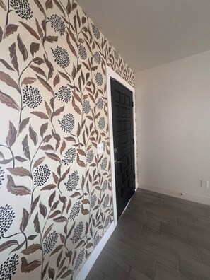 A hallway with patterned wallpaper and a dark door.