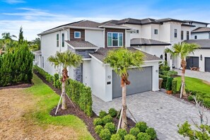 A modern residential building with a garage, surrounded by well-maintained lawns and palm trees. - Chic and Stylish 4 Bedroom Haven in Reunion Resort (Orlando)