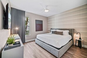 A modern bedroom with a large bed, a ceiling fan, a bedside table with a lamp, and a window with curtains. - Chic and Stylish 4 Bedroom Haven in Reunion Resort (Orlando)