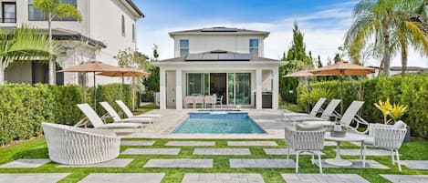 A modern house with a swimming pool, outdoor seating, and lush greenery.
