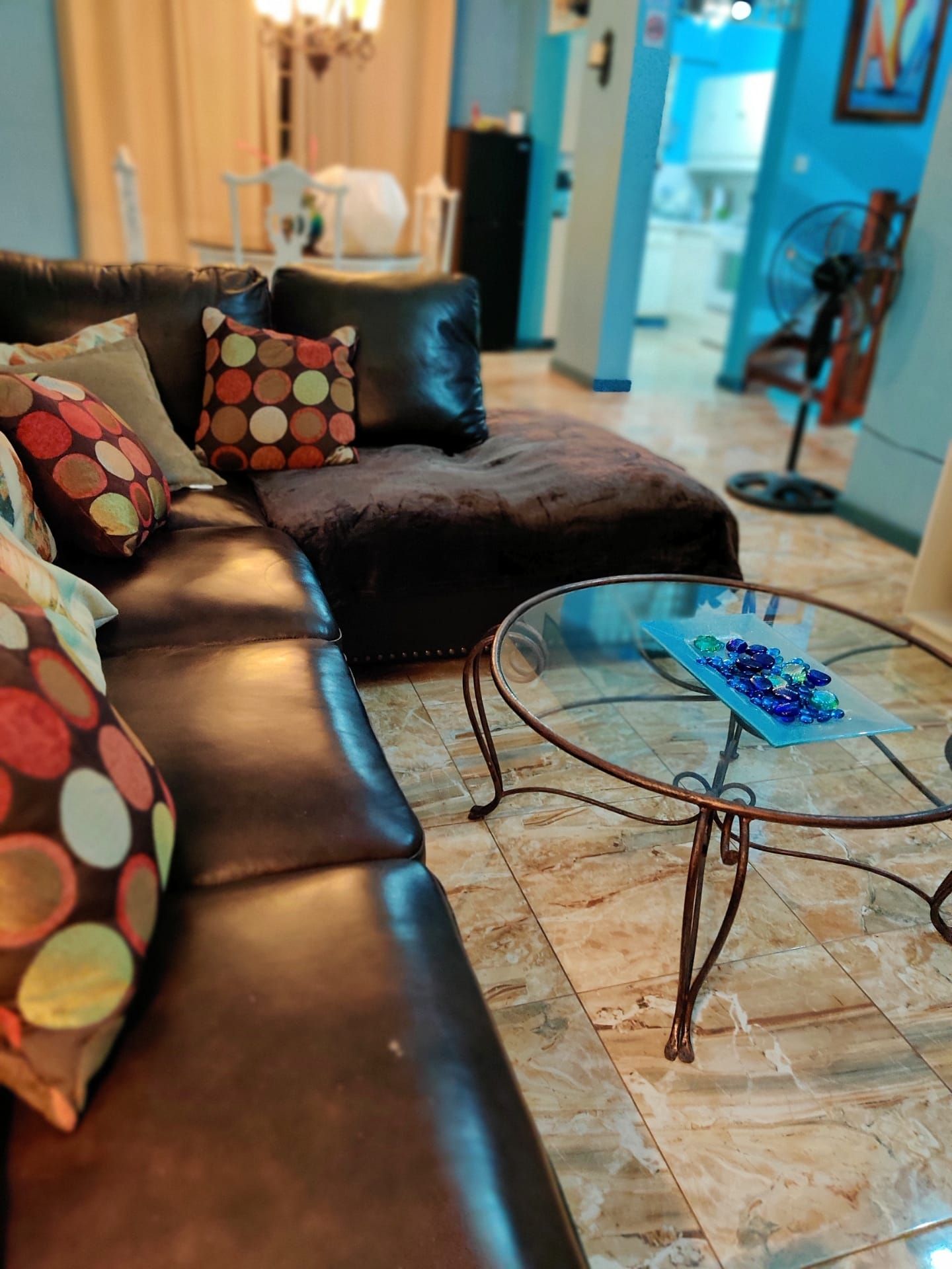 A living room with a leather sofa, a glass coffee table, and a patterned throw pillow.