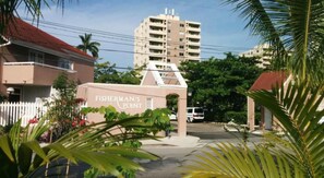 A building labeled "FISHERMAN'S POINT" with a white picket fence, palm trees, and a multi-story building in the background. - Searenity Beachfront View Hotel Apartment #29 Ocho Rios (Ocho Rios)
