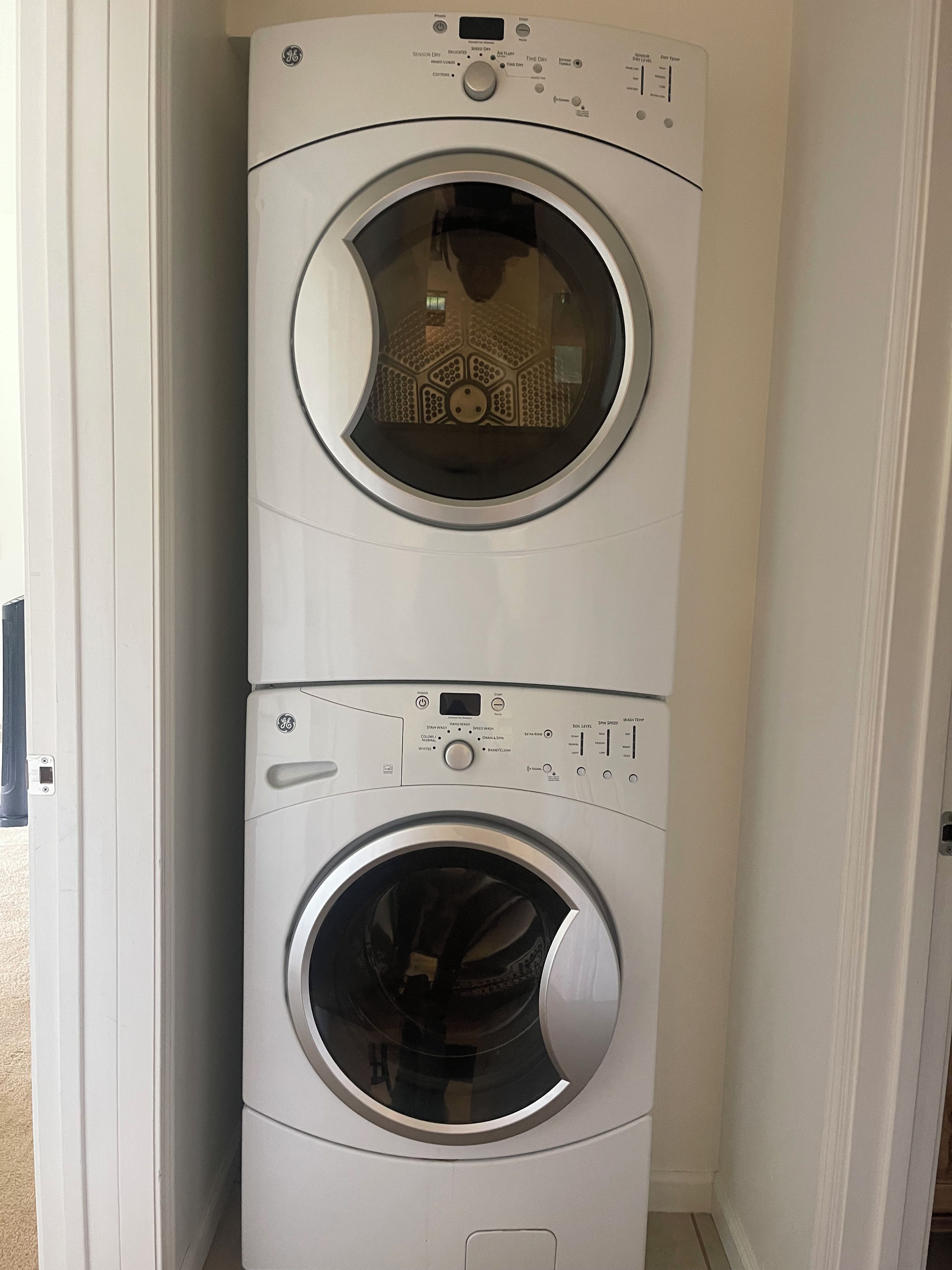 A stacked washer and dryer unit in a room with white walls and a door visible to the left.