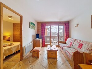 Ein gemütliches Zimmer mit einem Bett, einem Sofa, einem kleinen Tisch, einem Fernseher und einem Fenster mit Vorhängen.