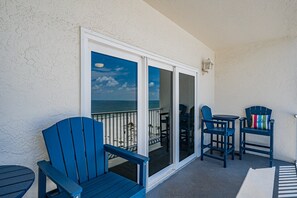 A balcony with a view of the ocean, featuring blue chairs and a small table. - 🐠Sea Breeze 505: Gulf-front |Madeira Beach| Pool| Hot Tub| John's Pass! (Madeira Beach)