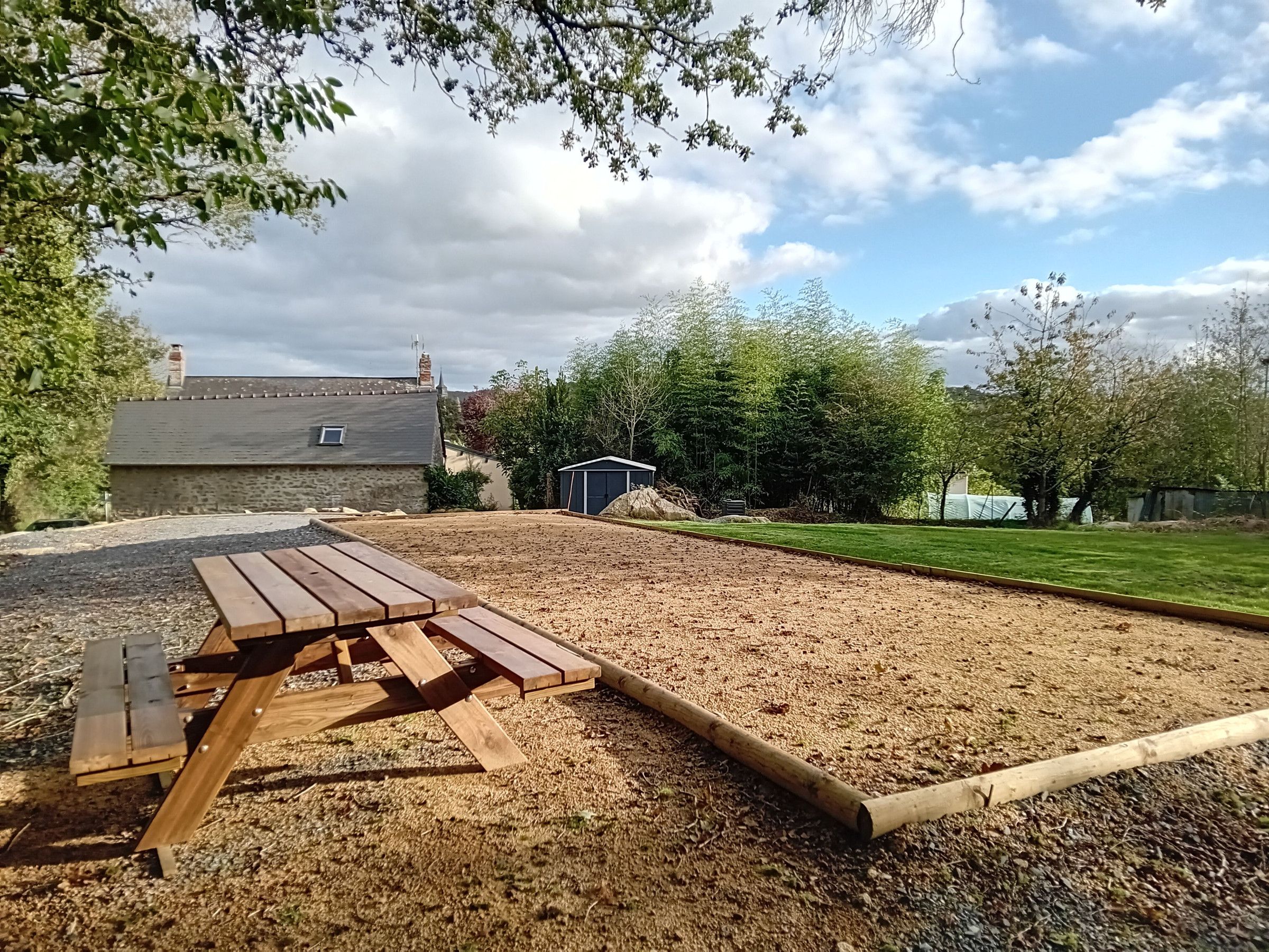 Een achtertuin met een houten picknicktafel, een tuinhuis en een gazon.