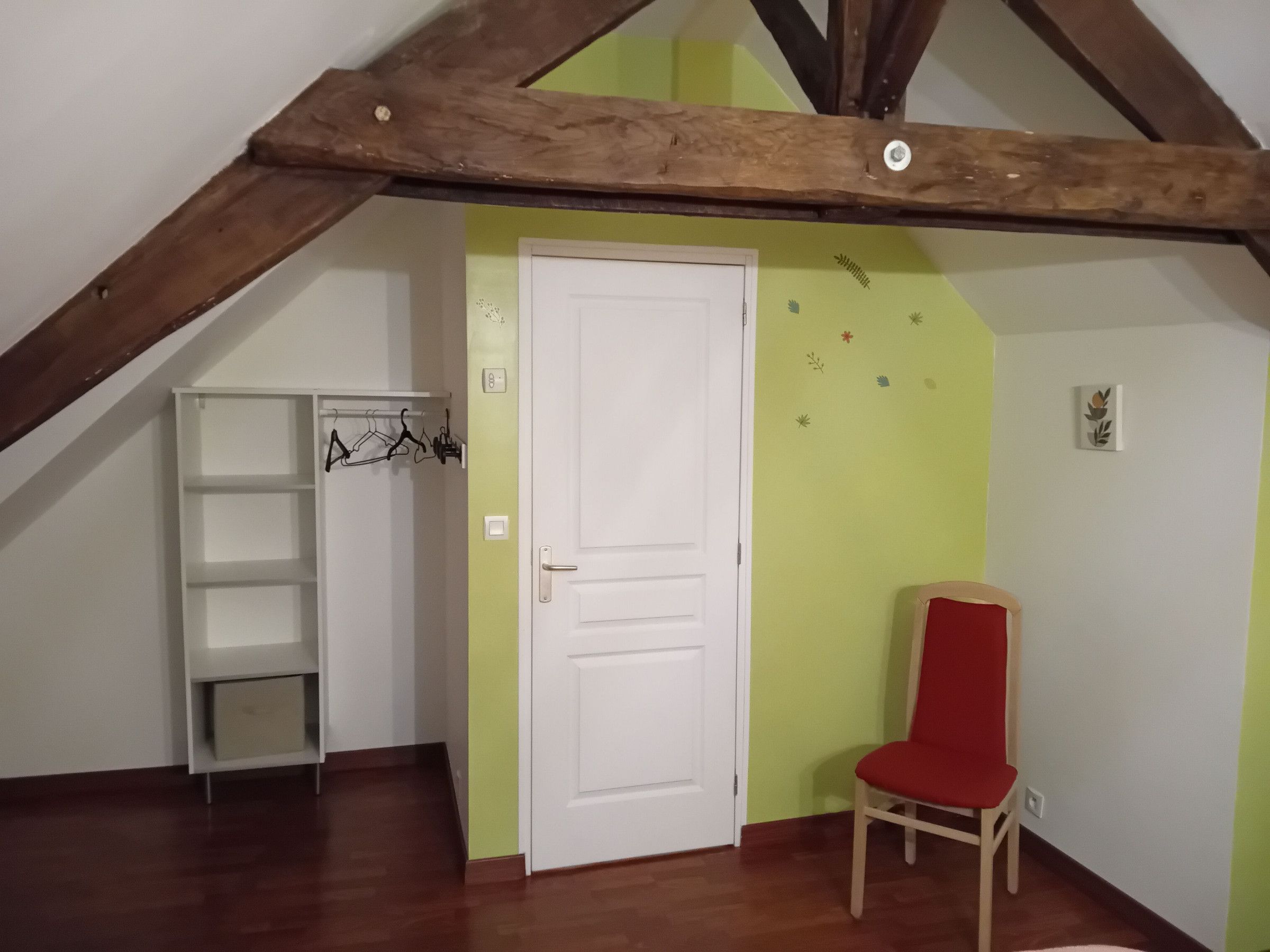 Ein Zimmer mit einer weißen Tür, einem roten Sessel, einer weißen Regaleinheit und einem Holzbalken an der Decke.