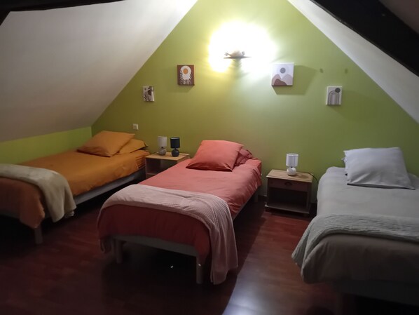 A triangular room with three beds, each with a different colored bedspread. There are bedside tables with lamps and wall art.