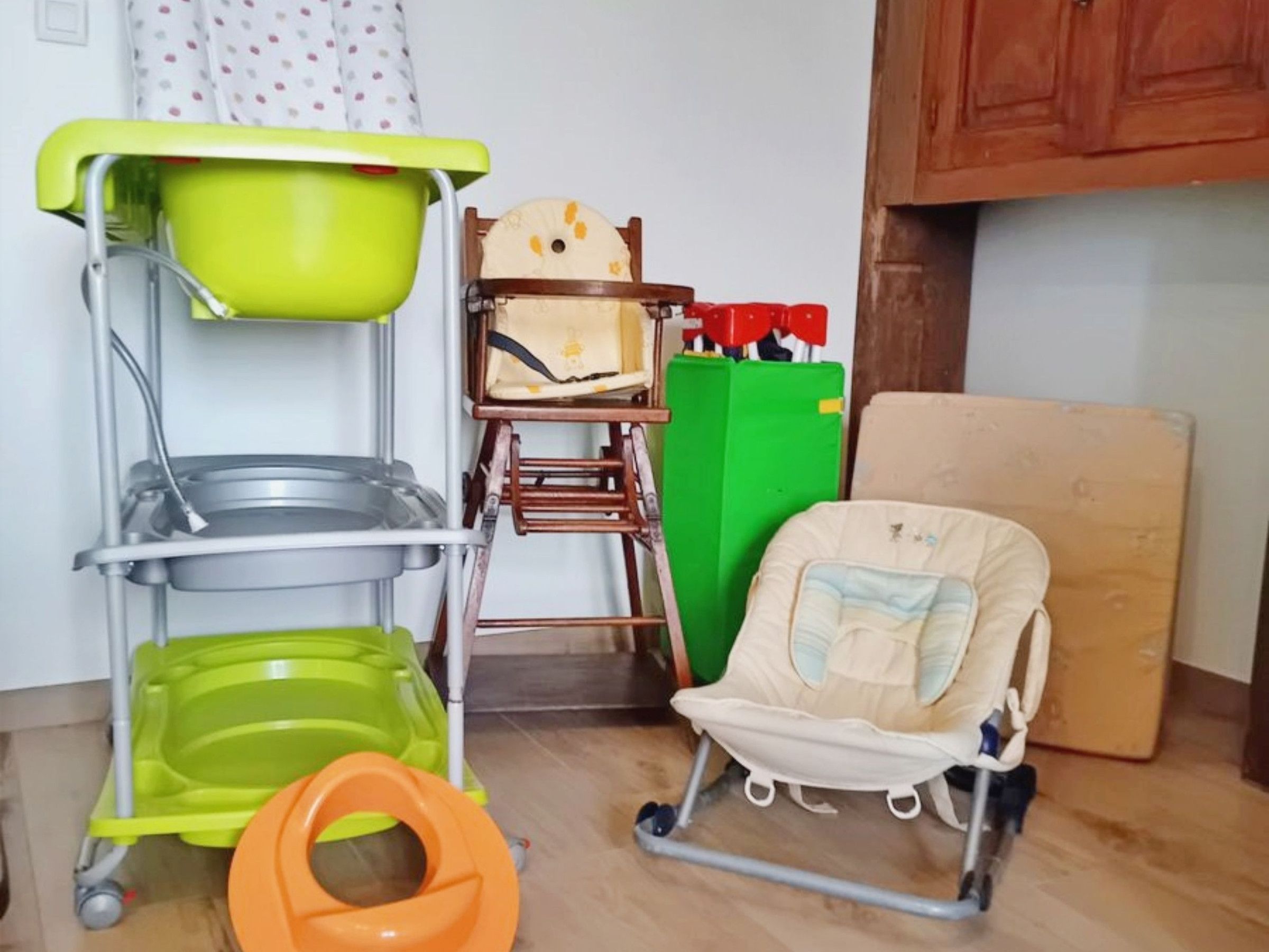 A room with a green and orange potty, a baby stroller, and a wooden cabinet.