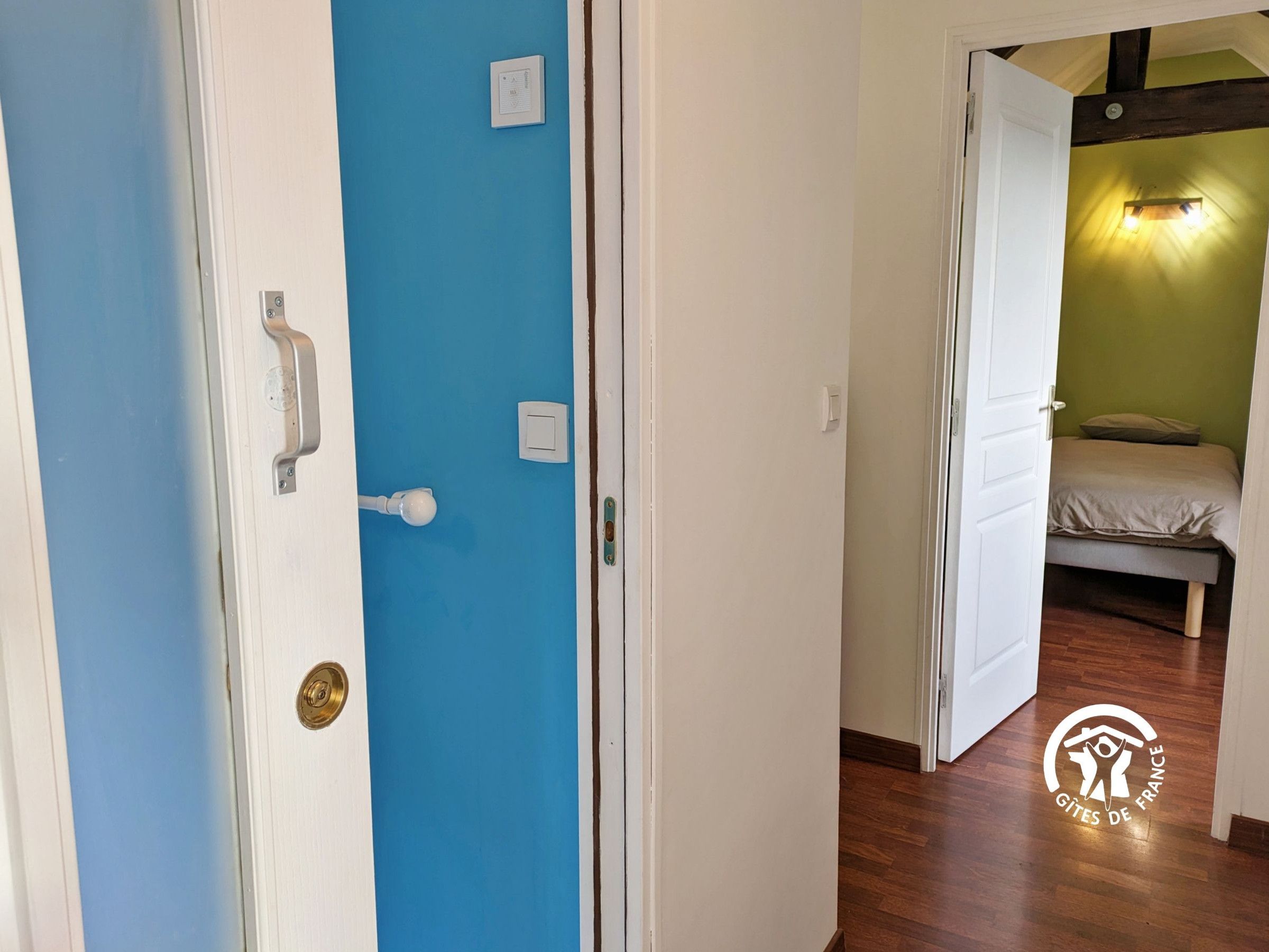 Una stanza con una porta blu, un letto a parete verde e un logo sul pavimento.
