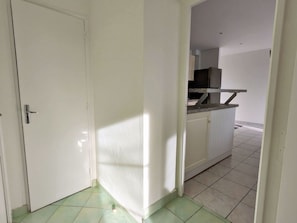 A corridor leading to a kitchen area with white walls and a tiled floor.