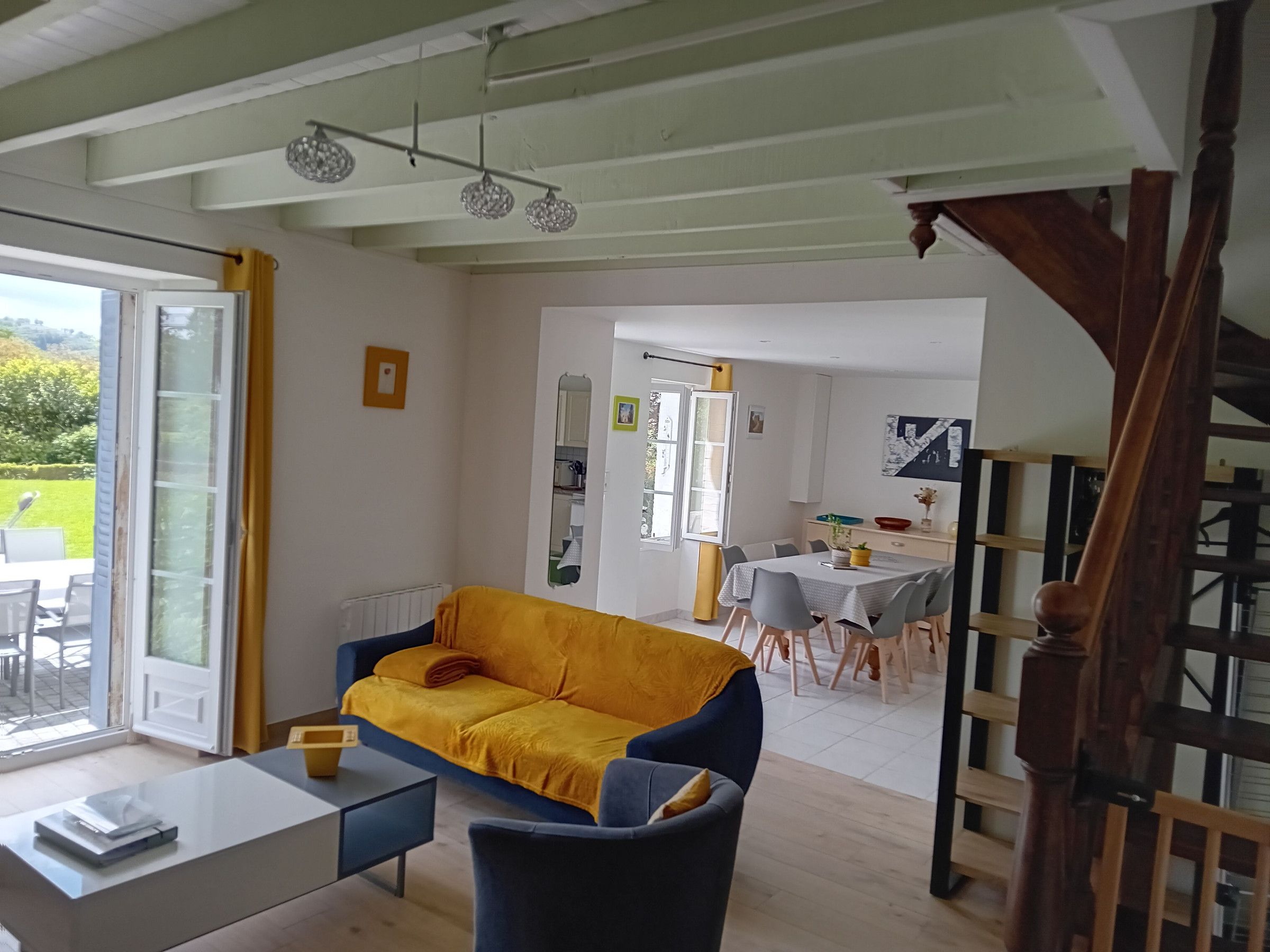 Sala de estar con sofá, una mesa de comedor y sillas. Se ve una escalera que conduce a otro nivel.