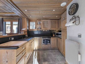 A kitchen with wooden cabinets, a microwave, an oven, and a clock on the wall. - Spacious apartment with South terrace - 6 guests (Méribel)