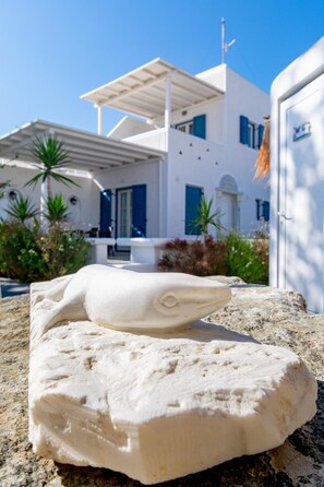 A white building with a flat roof and blue shutters, surrounded by greenery. - Gelos House (Mykonos)